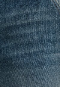 Denimtyg i en gradient från mörkblått till ljusare blått med märkbara sömmar. Har en texturerad yta med en svag lyster.