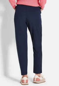 Marineblauwe broek met een taps toelopend ontwerp, gemaakt van een gladde stof. Draag het met lichtgekleurde sneakers met roze accenten.