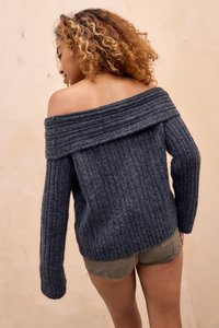 Pulover tricotat off-the-shoulder în gri închis, cu textură elastică, mâneci lungi și un decolteu larg. Asortat cu pantaloni scurți.