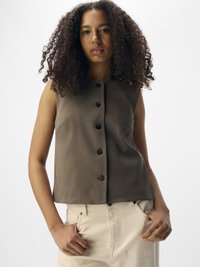 Haut sans manches marron avec un col rond, présentant une fermeture à boutons sur le devant et une texture lisse, associé à un pantalon de couleur claire.