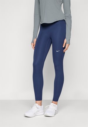 Jūras zilas leggingas ar gludu tekstūru, augstu jostasvietu un pieguļošu dizainu. Uz augšstilba ir diskrēta balta Nike logo.