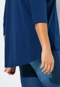 Marineblauw, lichtgewicht shirt met lange mouwen, een ronde zoom en opgerolde mouwen, gecombineerd met nauwsluitende blauwe jeans. Gladde textuur, casual ontwerp.