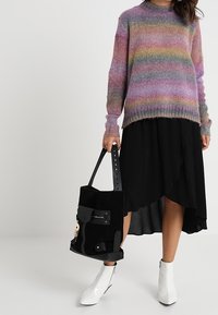 Monivärinen neulottu pusero, jossa vaakaraitoja, yhdistetty mustaan epäsymmetriseen helmaiseen hameeseen, mustaan mokkalaukkuun ja valkoisiin nilkkureihin.