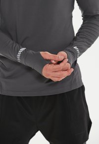 Donkergrijs sportshirt met lange mouwen en duimopeningen, voorzien van diagonale witte strepen op de manchetten, gecombineerd met zwarte shorts met zijzakken.