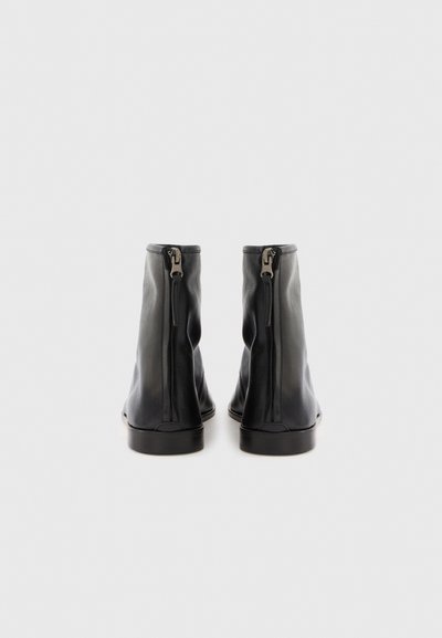 Stivali alla caviglia in pelle nera con una texture liscia, dotati di una cerniera sul retro e una punta arrotondata, con suola piatta.