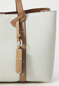 Lys grå vevd tote-bag med en strukturt finish, med en brun lærreim og et sølvfarget metalltilbehør.