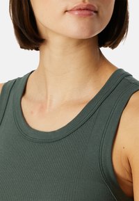 Grön ribbad tanktop med rund halsringning och breda axelremmar, med en texturerad tyg och slät yta.
