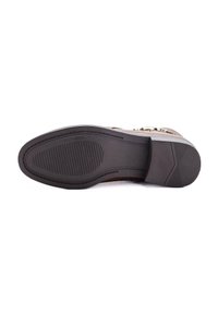 Suela de un zapato de vestir marrón con fondo de goma texturizada, bordes cosidos y un tacón bajo apilado, mostrado sobre un fondo blanco.