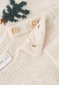 Krema pletena obleka z lesenimi gumbi, gumbnimi luknjami in delno črnim in rjavim vzorcem drevesa blizu ovratnika.