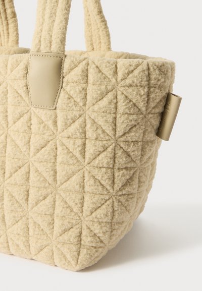 Sac fourre-tout beige matelassé avec une surface en laine texturée et deux poignées en tissu. Présente un accent en cuir et des motifs géométriques en triangles.