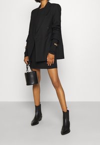 Czarna dwurzędowa marynarka noszona na czarnej, prążkowanej sukience, zestawiona z czarnymi botkami za kostkę i małą czarną torebką o konstrukcyjnym designie.