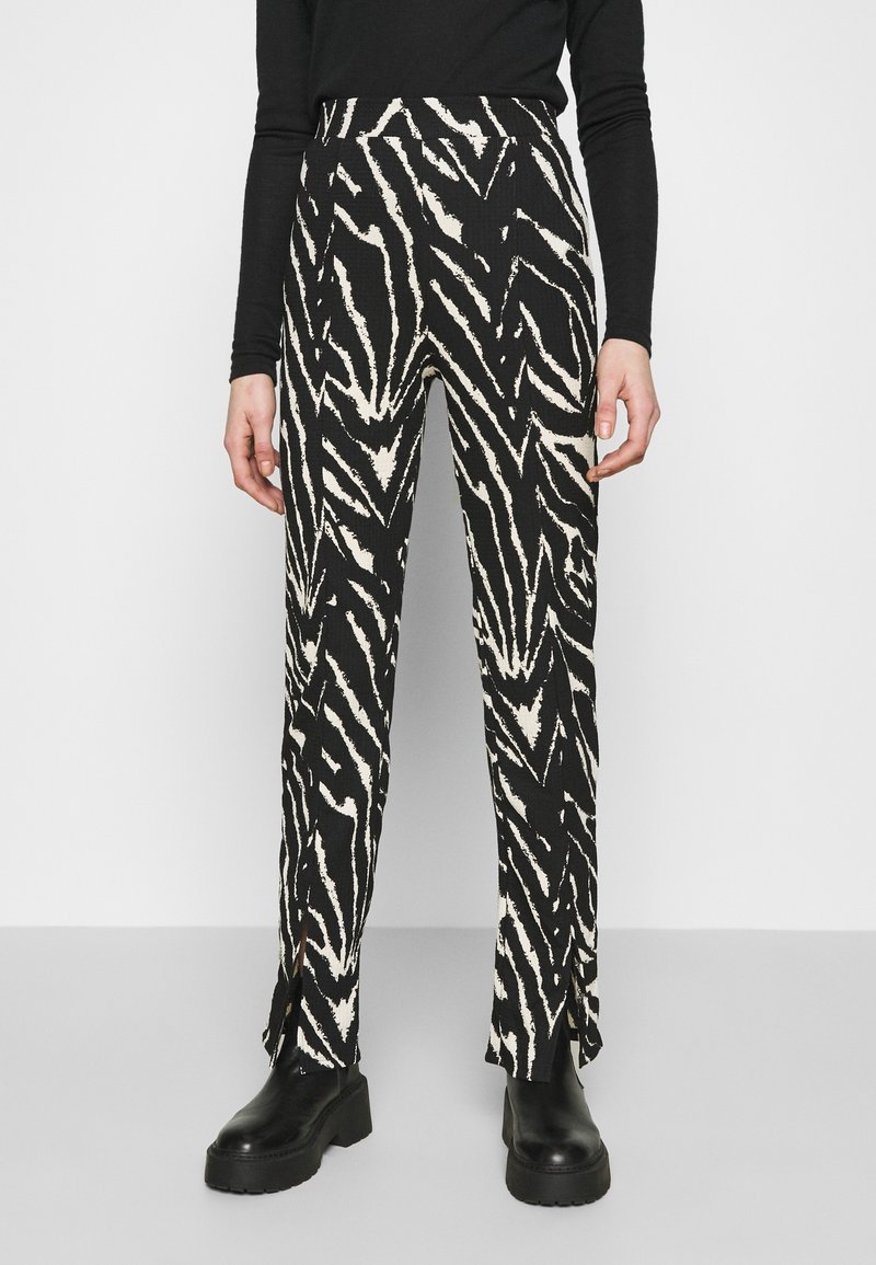 Czarno-kremowe spodnie w paski zebry z wysokim stanem, prostymi nogawkami i bocznymi rozcięciami u dołu. Połączone z czarnymi platformami.