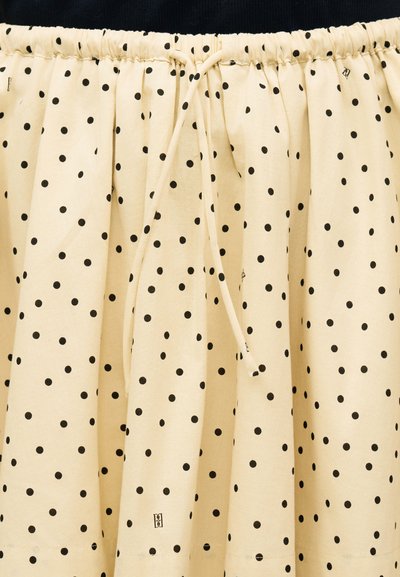 Κρεμ φούστα με μαύρες πουά, ελαστική μέση και κορδόνι δεμένο στη μέση μπροστά.