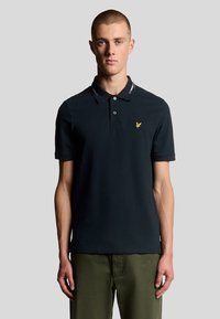 Polo shirt blu navy con colletto bottonato, caratterizzato da un'emblema di aquila gialla sul lato sinistro del petto e dettagli a righe sul colletto. Maniche corte.