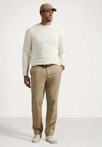 Beige genser med lange ermer, kremfargede bukser og lyse joggesko. Baseballcaps i beige med en logo. Enkelt, uformelt design.