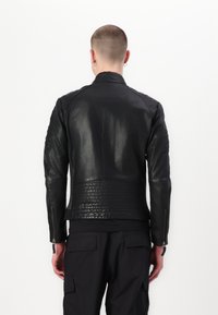 Giacca in pelle nera con vita testurizzata e maniche lisce, dotata di cerniere su entrambi i polsi e dettagli a costine sulle spalle.