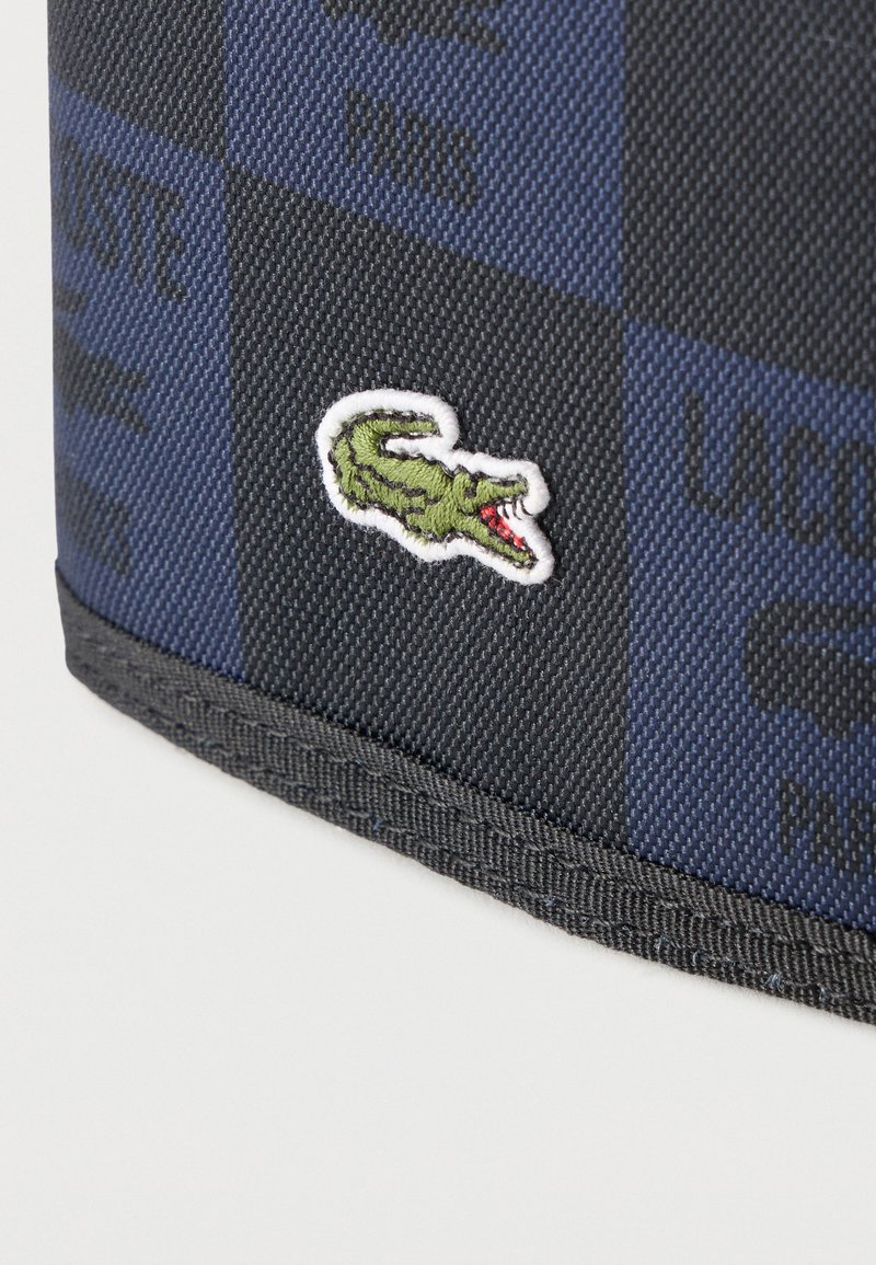 Primo piano di tessuto a scacchi blu e nero con logo coccodrillo verde ricamato e bordo nero cucito.