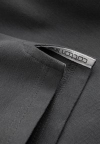 Close-up van een donkergrijze stoffen zak, met een klein wit label waarop "cotton line" staat, gedeeltelijk zichtbaar in de zak.