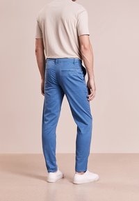 Světlemodré chinos kalhoty se slim fit střihem, bavlněný materiál, zadní kapsa a elastické manžety, kombinované s béžovým tričkem a bílými teniskami.