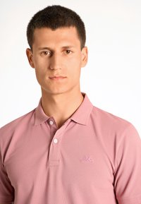 Polo rosa con tessuto texturizzato, chiusura a due bottoni e piccolo emblemma ricamato. Maniche corte e design del collo classico.