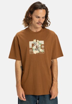 Bruine katoenen t-shirt met korte mouwen, met een bloem- en grafisch ontwerp in het wit en groen in het midden. Casual, ontspannen pasvorm.