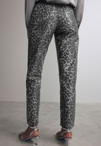 Pantalons à imprimé léopard gris avec une coupe slim, dotés de deux poches arrière et d'une texture lisse et légèrement brillante. Associés à des sandales métalliques.