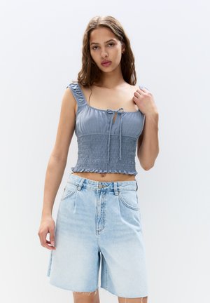 Top court smocké bleu avec lien ajustable au cou, associé à un short en denim bleu clair. Texture de tissu naturel ; coupe décontractée.