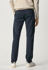 Mörkblå chinos med slim fit, i bomullsmaterial, bakfickor med accent i guldknappar, kombinerat med vita sneakers.