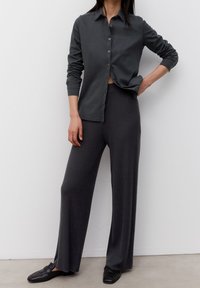 Camicia button-up grigia scura con colletto, abbinata a pantaloni grigi a gamba larga e a costine. Modello con scarpe nere slip-on. Tessuto liscio, vestibilità rilassata.