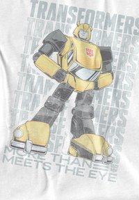 Transformers graphic t-shirt featuring a yellow robot with black accents, standing posed. Background text reads "Transformers" and "More Than Meets the Eye."