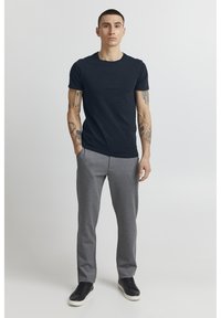 Marineblå t-skjorte med kort erm og en subtil hevet logo, kombinert med grå joggebukser og svarte joggesko, som skaper en uformell stil.