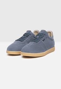 Zapatillas de ante azul con punta redonda, cordones planos y suela de goma. Presentan un mínimo de costuras y un suave forro interior.