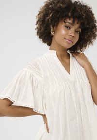 Blusa bianca leggera con maniche corte a palloncino, righe verticali, pois sottili, e colletto a notched con bordi scallop.