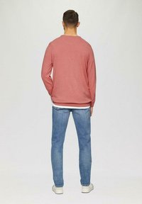 Rotes Langarmhemd aus Baumwollmix, mit Rundhalsausschnitt. Kombiniert mit hellblauen Jeans, lässiger Schnitt, und weißen Sneakern.