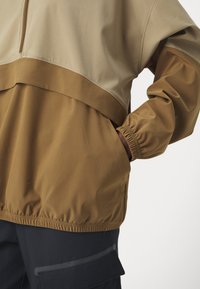 Pruun ja beež pullover-jakk elastsete mansettide ja äärega, millel on pooltõmbele ja eesmine tasku. Valmistatud siledast ja kergest kangast.