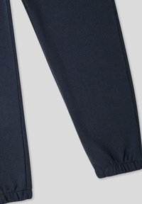 Granatowe spodnie dresowe wykonane z miękkiego, elastycznego materiału; elastyczne mankiety przy kostkach; gładka faktura z delikatnym połyskiem i bez wzorów.