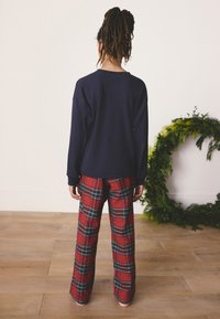 Navy long-sleeve top paired with red plaid pants featuring green and white lines. Relaxed fit with loose sleeves, plain back design.