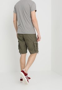 Pantaloni cargo color khaki con più tasche laterali e risvolti, abbinati a una maglietta grigia e scarpe da ginnastica rosse con dettagli bianchi.