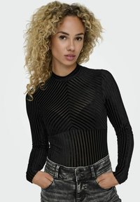 Top nero a maniche lunghe con tessuto a strisce trasparenti e sezioni nere opache. Abbinato a jeans neri sbiaditi a vita alta con chiusura a doppio bottone.