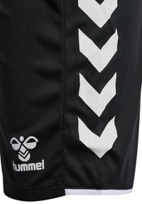 Nahaufnahme schwarzer Sportshorts mit einem weißen Hummel-Bienenlogo und vier weißen, nach unten zeigenden Chevron-Streifen an der Seite.