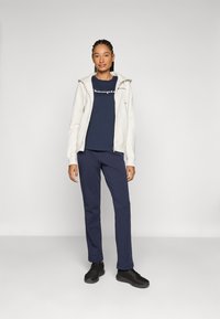 Hvit zip-up hettegenser, marineblå crew-neck t-skjorte med tekst, marineblå joggebukser og svarte joggesko. Glatt stoff med en avslappet passform.