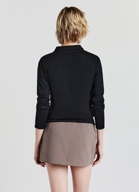 Top nero a maniche lunghe con colletto, abbinato a una gonna beige. Il top presenta una texture liscia, mentre la gonna ha un design strutturato.