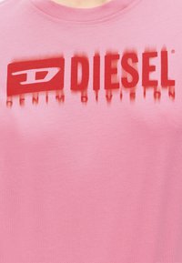 Ροζ πουκάμισο με κόκκινο λογότυπο Diesel και το κείμενο «Denim Division» τυπωμένο κάτω από το λογότυπο.