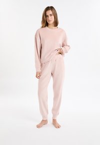 Ensemble de détente deux pièces rose clair en tissu texturé. Le haut présente un col rond et le pantalon est doté de poignets et d'une taille élastiques.