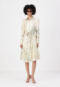 Abito camicia in tessuto leggero, con una stampa botanica in tonalità di verde e beige. Parte anteriore con bottoni, vita cinchata e maniche lunghe.