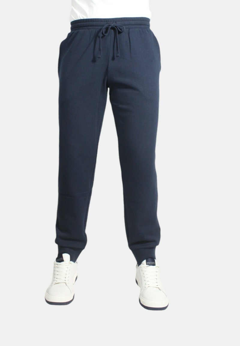 Pantaloni jogger navy con cintura elastica, cordino, tasche laterali e polsini affusolati, abbinati a sneakers bianche.