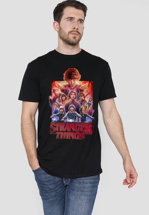 Black cotton t-shirt featuring a colorful graphic of characters from "Stranger Things" in a comic-style design, with bold red text.
