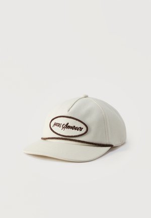 Cappellino da baseball beige con testo ricamato marrone "hotel Americer" all'interno di un bordo ovale e dettaglio a corda marrone sopra la visiera.