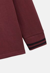 Chemise à manches longues bordeaux avec une texture douce ; présente des accents rayés navy au niveau des poignets ; coupe classique et design de manches à poignets.