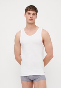 Weißes Tanktop aus Baumwollstoff mit rundem Halsausschnitt, schlankem Schnitt und minimalen Nähten. Kombiniert mit grauen gestreiften Slips.